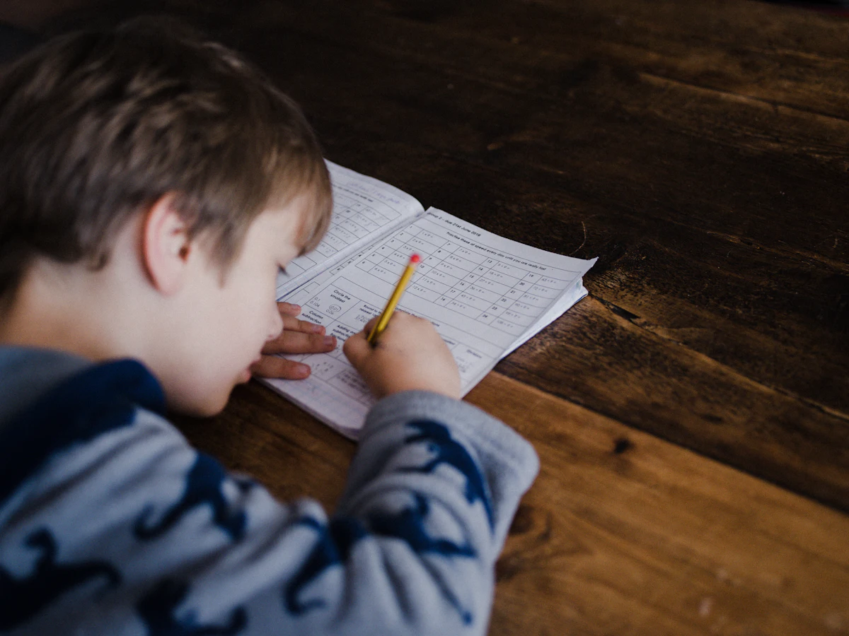 A child writing in a workbook at a wooden table